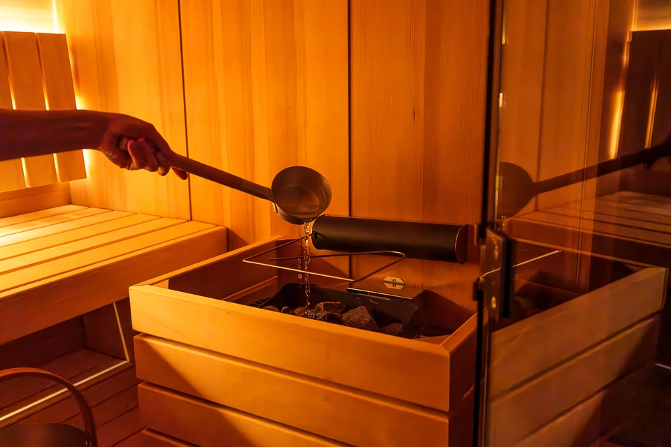 A hand pours water onto the sauna heater at Peterhof